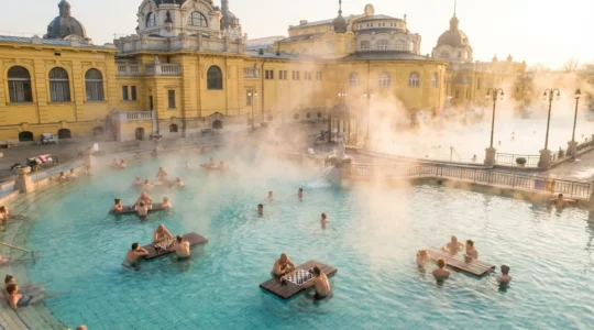 Vue panoramique d'un bassin thermal extérieur avec des baigneurs jouant aux échecs sur des plateaux flottants dans l'eau chaude fumante